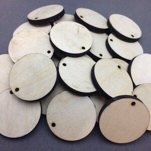 May include: A pile of round, unfinished wooden circles with black edges and a small hole in the center. The circles are arranged in a random pattern.