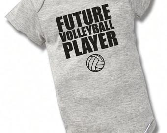 May include: A light gray short-sleeve baby bodysuit featuring the black text FUTURE VOLLEYBALL PLAYER printed on the chest, accompanied by a small black graphic of a volleyball positioned directly below the text.