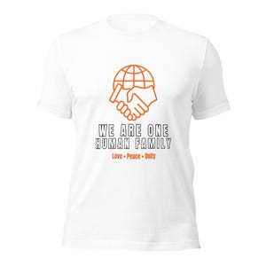 May include: A white short-sleeved t-shirt featuring an orange graphic of a globe and a handshake. Below the graphic, the text reads WE ARE ONE HUMAN FAMILY in black, followed by the orange text Love • Peace • Unity centred on the chest.