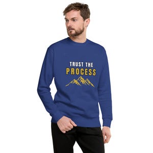 May include: A blue sweatshirt with the text "TRUST THE PROCESS" in white and gold, with a gold mountain graphic below. The sweatshirt is a solid blue color.