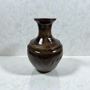 以下が含まれることがあります： テクスチャ加工された表面を持つ茶色のセラミック花瓶。花瓶は丸みを帯びたボディと細い首を持っています。色は暗く土のような茶色で、光沢のある仕上がりです。花瓶は家の装飾に適しています。