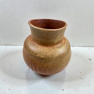 Peut inclure: Petit vase en céramique fait à la main, avec un corps arrondi et un bord légèrement évasé. Le vase présente un aspect tacheté et terreux avec un dégradé de couleurs, allant du brun chaud à une teinte rouge-orangé. L'intérieur est d'une nuance de brun plus foncée.