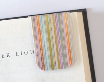 May include: A colourful striped bookmark with a clear plastic cover. The bookmark is placed on a book with the text "Chapter Eight" visible.