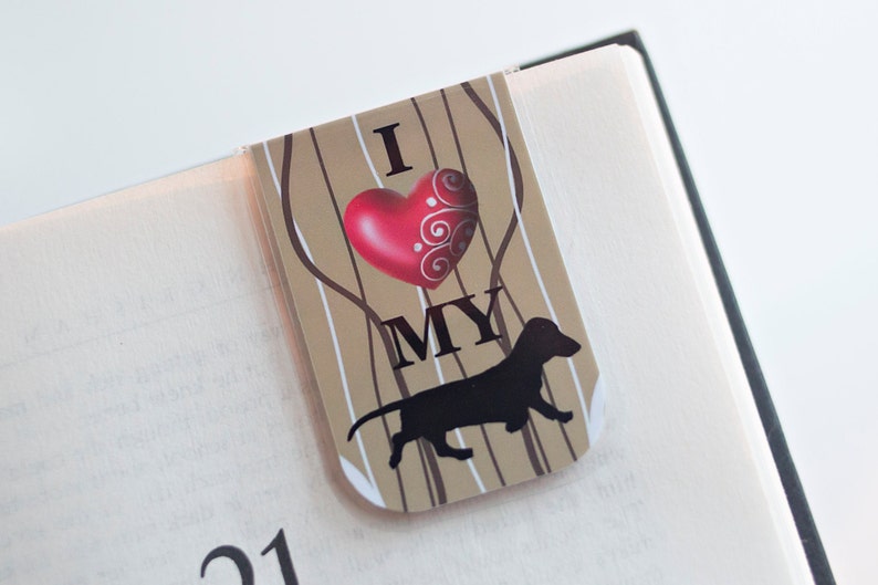 May include: A brown and white bookmark with a red heart and the text "I love my" and a black silhouette of a dachshund.