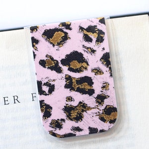 Puede incluir: Marcapáginas magnético de leopardo rosa y dorado. El marcapáginas está sujeto a un libro con el texto "CHAPTER F" visible.