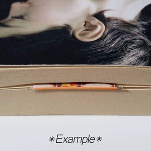 May include: Close-up of a book's spine with a colorful, striped bookmark sticking out. The bookmark is orange, yellow, red, and black.