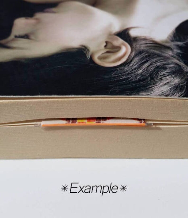 May include: Close-up of a book's spine with a colorful, striped bookmark sticking out. The bookmark is orange, yellow, red, and black.