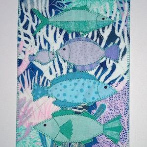 May include: A fabric art piece with four fish appliquéd in shades of blue, teal, and purple. The fish are set against a background of coral and abstract patterns in blue, pink, and white. The edges are finished with green stitching.