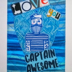 May include: A blue and white quilted fabric art piece with a sailor illustration and the text "I love you Captain Awesome".