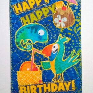 May include: A colorful birthday card with a blue background and yellow stitching. The card features a green chameleon, a blue parrot, and a yellow and orange drink with a pink umbrella. The text "Happy Happy Birthday!" is written in yellow letters.
