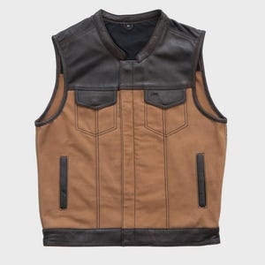 May include: A brown and black leather vest with a collared neckline and two front pockets. The vest has a brown canvas body with black leather accents on the shoulders, pockets, and trim. The vest is sleeveless and has a classic biker style.