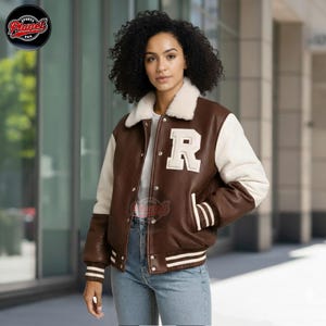 May include: A brown and cream varsity jacket with a white 'R' patch on the chest. The jacket has a cream-colored collar and sleeves, with white stripes on the cuffs and hem. The jacket is made of leather and has a button-up front.
