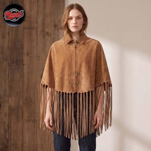 Women's genuine suede leather fringe western boho cape poncho — A tan suede cape featuring a full-length front zipper, a classic collar, and long fringe detailing along the hemline. The garment is constructed with visible stitching and a structured s