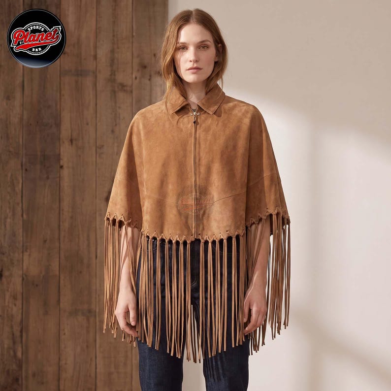Women's genuine suede leather fringe western boho cape poncho — A tan suede cape featuring a full-length front zipper, a classic collar, and long fringe detailing along the hemline. The garment is constructed with visible stitching and a structured s