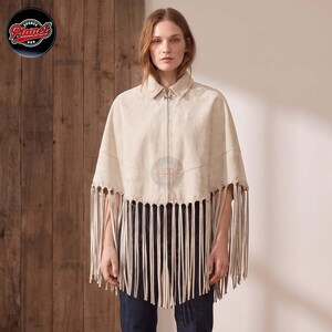 Women's genuine suede leather fringe western boho cape poncho — A beige suede cape featuring a collared neckline, a central silver-toned zipper closure, and long fringe detailing along the bottom hem. The garment is worn over dark blue denim jeans, s