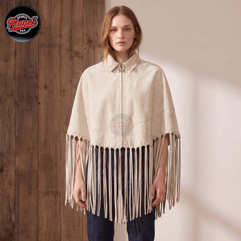 Women's genuine suede leather fringe western boho cape poncho — A beige suede cape featuring a collared neckline, a central silver-toned zipper closure, and long fringe detailing along the bottom hem. The garment is worn over dark blue denim jeans, s
