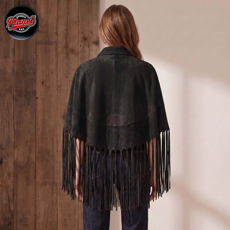 Women's genuine suede leather fringe western boho cape poncho — A dark charcoal gray suede cape featuring a scalloped hemline adorned with long, thin fringe detailing that extends from the back. The garment is worn over dark blue denim jeans, showcas