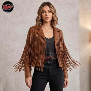 Puede incluir: Una chaqueta marrón con largos flecos en el pecho y las mangas, cuello con solapas y cierre frontal de botones. La chaqueta se lleva sobre una camiseta negra y pantalones negros. Se ve un logotipo circular con el texto Sports Planet.