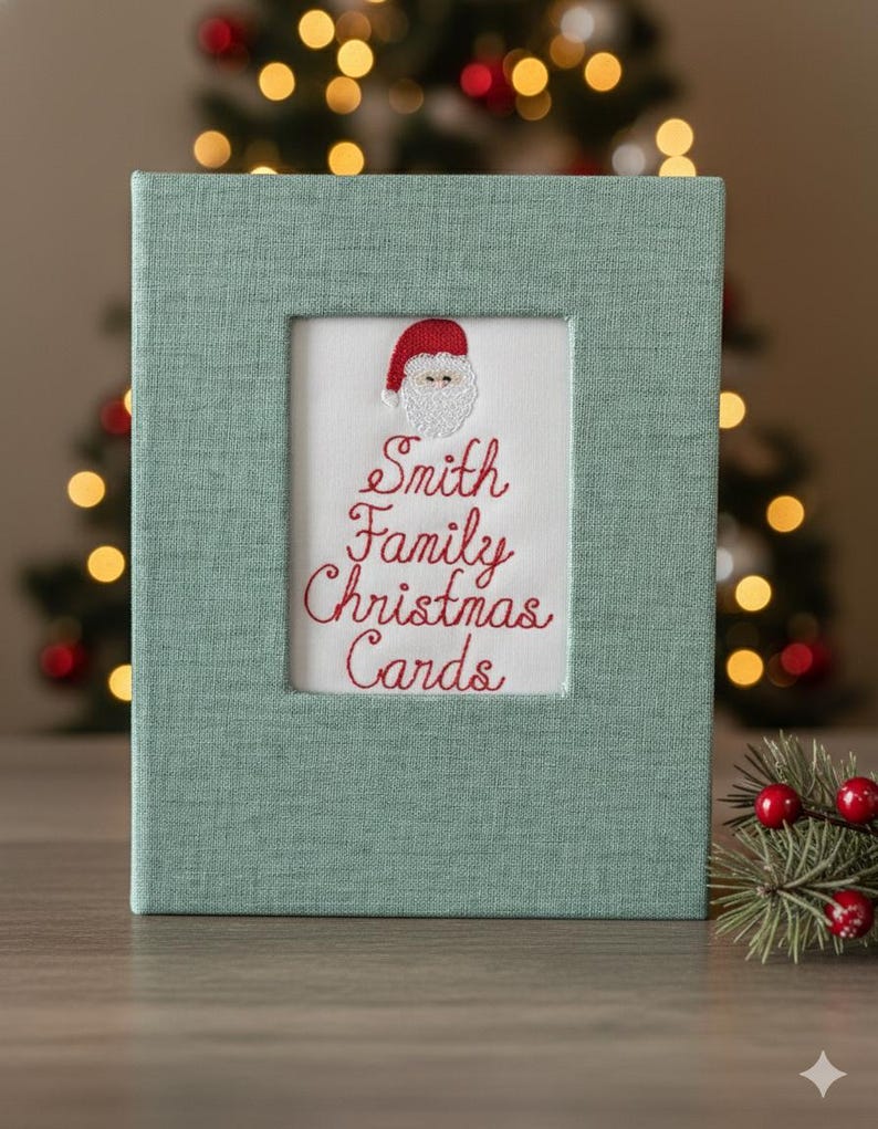 May include: A rectangular, light green fabric-covered box with a rectangular opening. The opening reveals a white background with red embroidered text that reads "Smith Family Christmas Cards" and a Santa Claus design.
