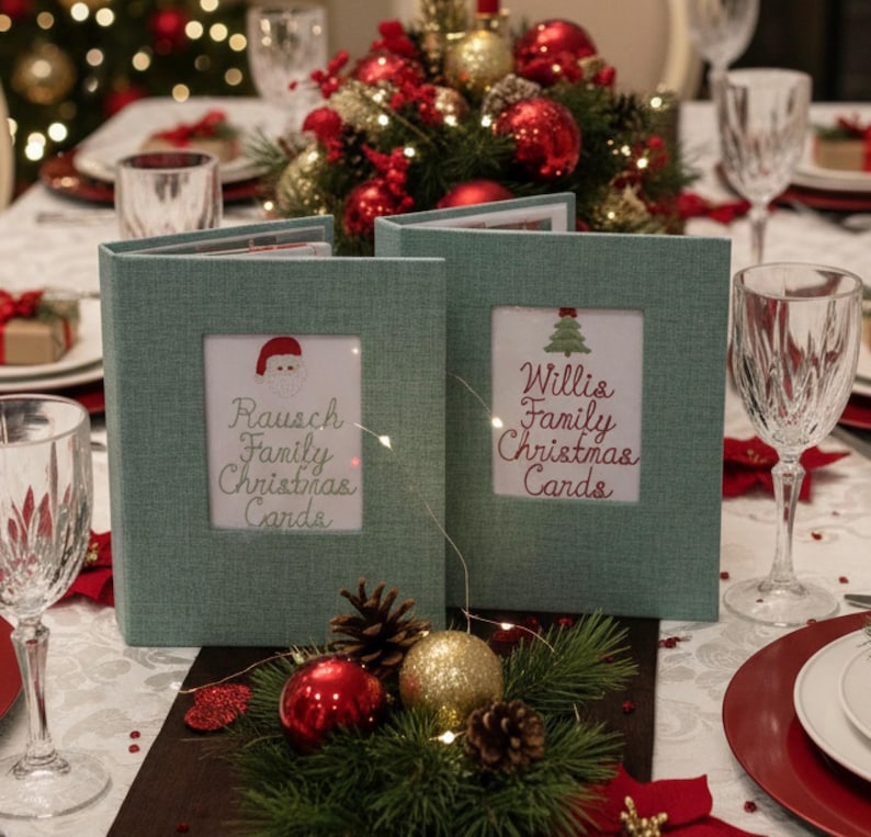 May include: Two teal fabric Christmas card holders with framed inserts. One has a Santa hat graphic and the text "Rausch Family Christmas Cards." The other has a Christmas tree graphic and the text "Willis Family Christmas Cards." The holders are on a decorated table.