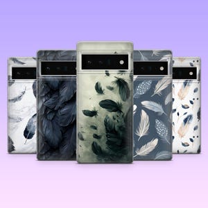 May include: A collection of five phone cases with feather designs. The cases feature various color schemes, including white, navy, and gray, with detailed feather illustrations. The cases are arranged in a row against a gradient purple background.