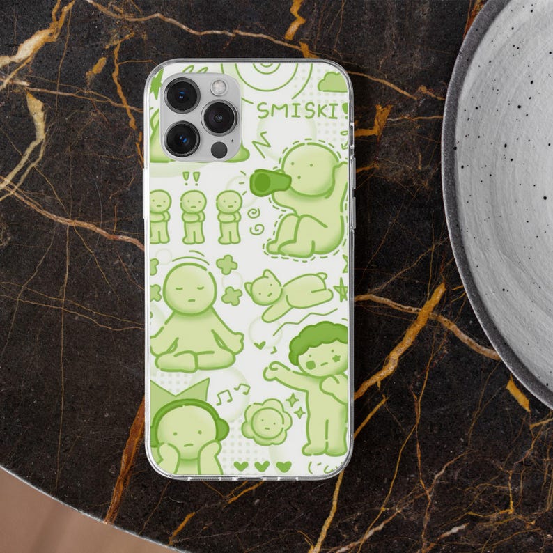 Puede incluir: Una funda transparente para tel&eacute;fono con una ilustraci&oacute;n verde claro de figuras de dibujos animados y la palabra "SMISKI". El dise&ntilde;o incluye varias poses de las figuras, notas musicales, corazones y nubes. La funda est&aacute; sobre una superficie oscura y estampada.