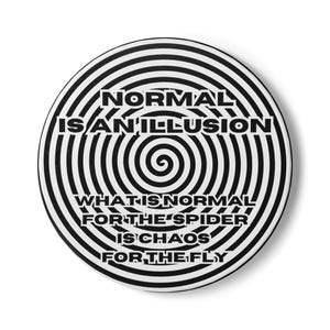 May include: A round, white button with a black and white spiral design. The text "NORMAL IS AN ILLUSION" and "WHAT IS NORMAL FOR THE SPIDER IS CHAOS FOR THE FLY" is printed in black.