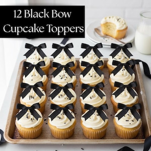 May include: A display of cupcakes with white icing and black bow decorations. The cupcakes are arranged on a tray. The image includes the text "12 Black Bow Cupcake Toppers" at the top, indicating the product.