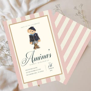 May include: Amina's first birthday invitation with a teddy bear illustration. The invitation features a pink and white striped background, a cream-colored central panel, and gold accents. The text includes the name "Amina's", the date, time, and location.