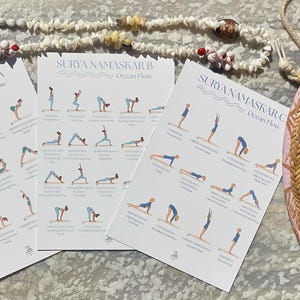 Peut inclure: Trois cartes blanches avec des poses de yoga intitulées "Surya Namaskar A, B, C Ocean Flow" sont affichées. Un chapeau de paille avec une bordure rose et un collier de coquillages sont également visibles.