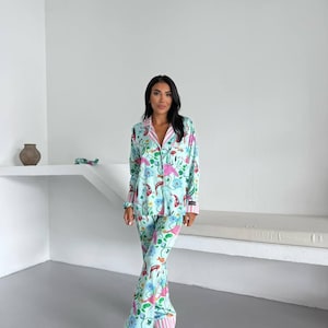 May include: A light blue pajama set with a floral and fish pattern. The long-sleeved top and pants feature pink and white striped trim. The pajamas have a button-down shirt and wide-leg pants.