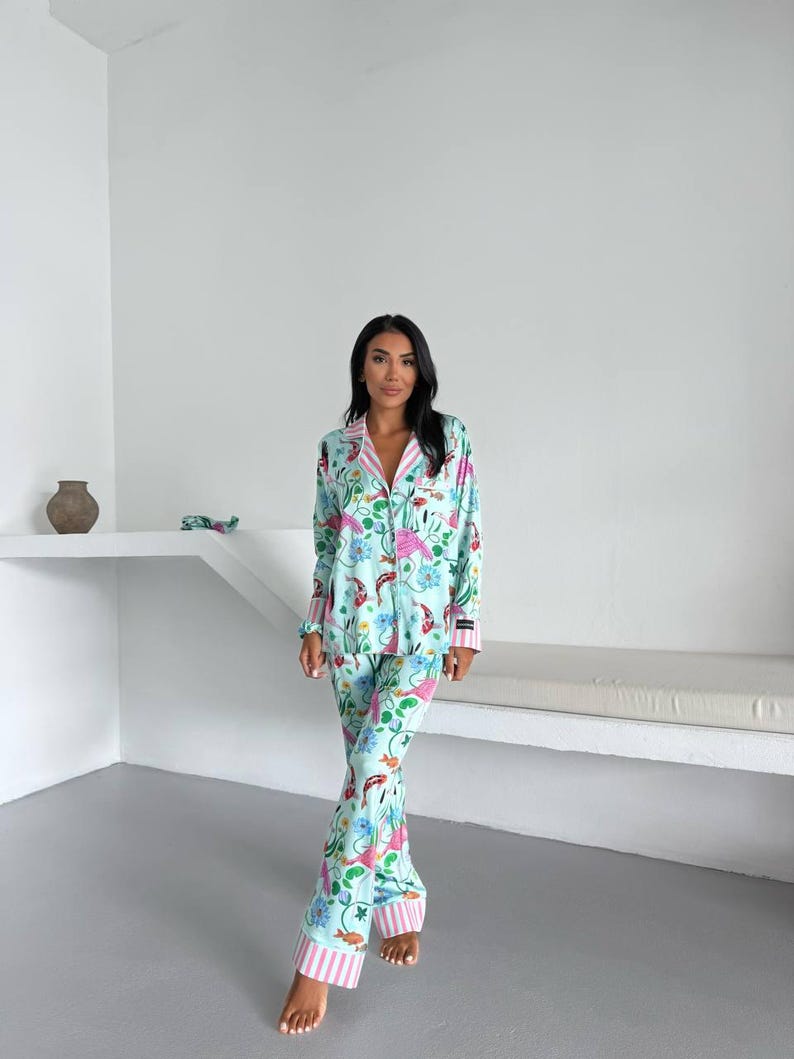 May include: A light blue pajama set with a floral and fish pattern. The long-sleeved top and pants feature pink and white striped trim. The pajamas have a button-down shirt and wide-leg pants.