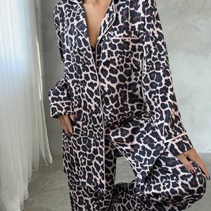 May include: A two-piece leopard print pajama set. The long-sleeved top and pants feature a brown and black animal print pattern with pink trim. The pajamas have a classic button-down design.