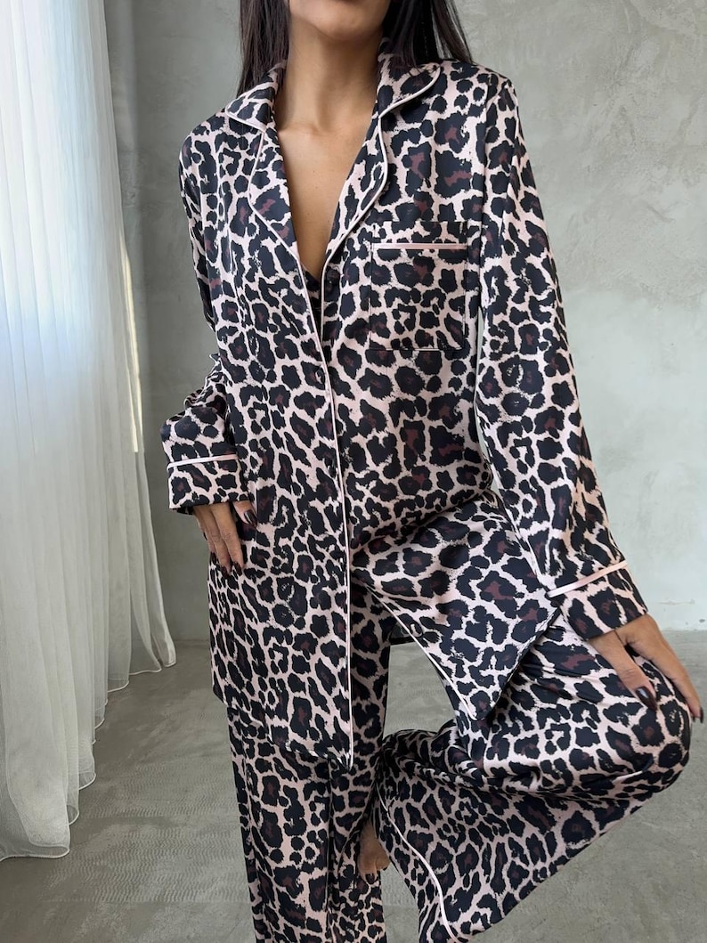 May include: A two-piece leopard print pajama set. The long-sleeved top and pants feature a brown and black animal print pattern with pink trim. The pajamas have a classic button-down design.