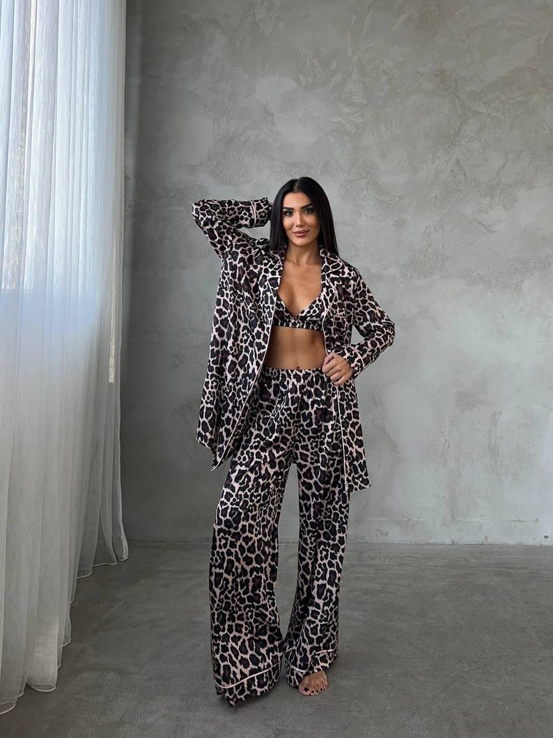 Pode incluir: Um conjunto de pijama com estampa de leopardo de tr&ecirc;s pe&ccedil;as. O conjunto inclui uma jaqueta de manga comprida, um bralette e cal&ccedil;as de perna larga. O pijama &eacute; em estampa animal marrom e preta com acabamento rosa claro.