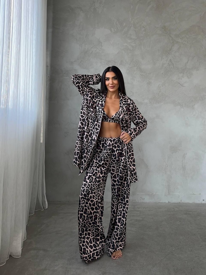 May include: A three-piece leopard print pajama set. The set includes a long-sleeved jacket, a bralette, and wide-leg pants. The pajamas are in a brown and black animal print with a light pink trim.