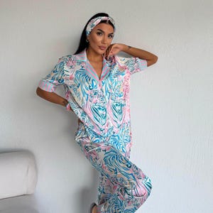 Könnte beinhalten: Ein zweiteiliger Schlafanzug mit passendem Stirnband mit Tigerdruck in Blau-, Rosa- und Weißtönen. Das kurzärmelige Oberteil hat einen Kragen und einen rosa-blau gestreiften Besatz. Die Hose ist lang und locker geschnitten.