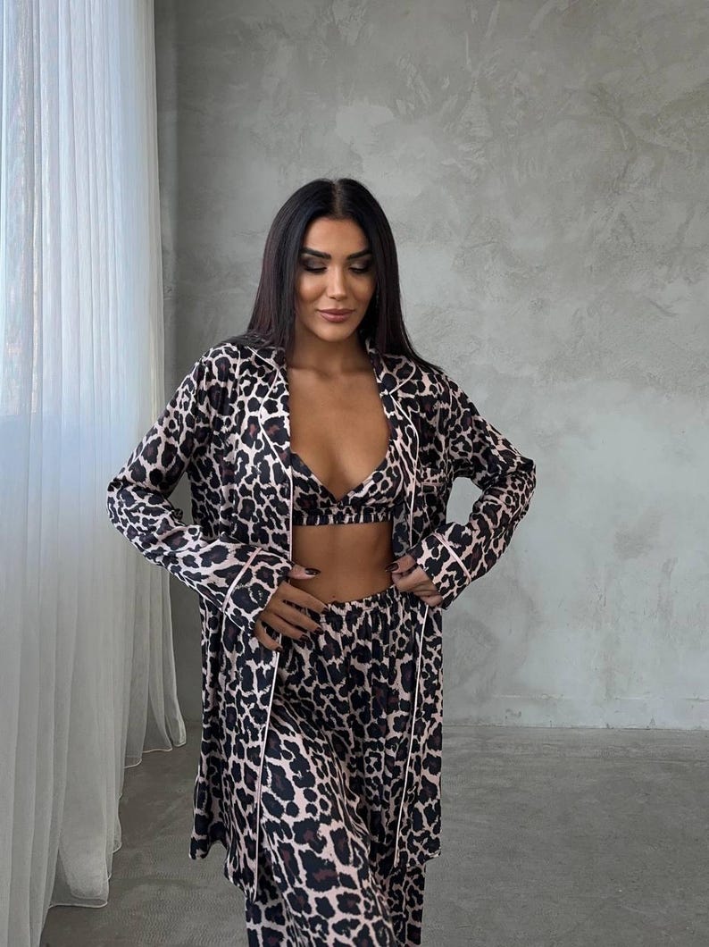 May include: A three-piece leopard print pajama set. The set includes a long-sleeved robe, a bralette, and matching pants. The pajamas are in a brown and black animal print with light pink trim.
