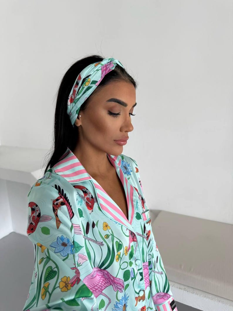 May include: A light blue pajama set with a matching headband. The set features a floral and animal print with pink flamingos, koi fish, and lotus flowers. The pajama top has pink striped trim.