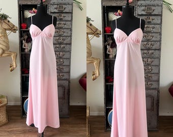 May include: A light pink, floor-length slip dress with spaghetti straps and a gathered bust. The dress is displayed on a black mannequin. The dress has a simple, elegant design, perfect for vintage-inspired fashion or lingerie.