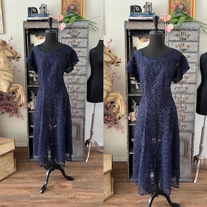 Könnte beinhalten: Ein marineblaues Spitzenkleid mit kurzen Ärmeln und ausgestelltem Rock wird auf einer schwarzen Schneiderpuppe präsentiert. Das Kleid hat einen Rundhalsausschnitt und ein zartes Blumenmuster. Das Kleid ist im Vintage-Stil.