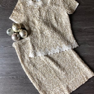 May include: A two-piece outfit in a cream color with a rose-like textured fabric. The top has short sleeves and a round neckline. The skirt is a pencil skirt.