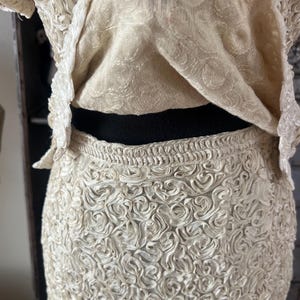 May include: A white skirt made of fabric with a rosette pattern. The skirt is fitted and has a high waist.