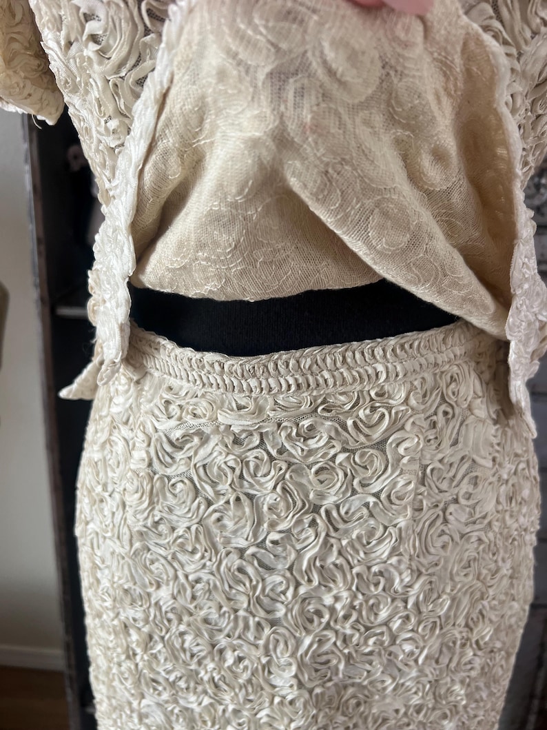 May include: A white skirt made of fabric with a rosette pattern. The skirt is fitted and has a high waist.