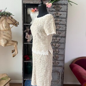 May include: A white dress with a floral pattern and a white lace trim. The dress has short sleeves and a fitted skirt.