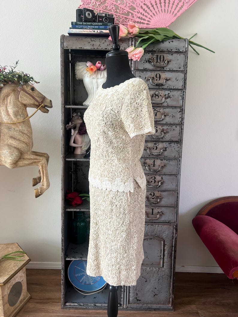May include: A white dress with a floral pattern and a white lace trim. The dress has short sleeves and a fitted skirt.