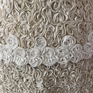 May include: A close-up of a white fabric with a textured pattern of small, raised rosettes. The fabric has a delicate, feminine look.