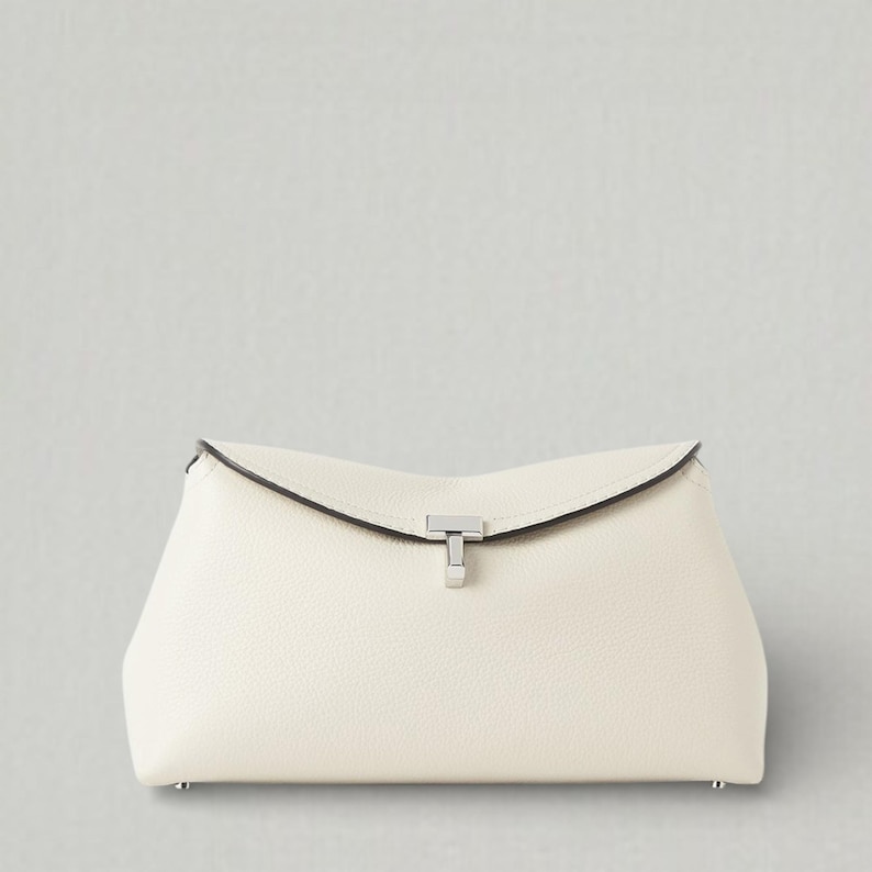 Pu&ograve; includere: Pochette color crema con forma rettangolare e patta superiore curva. La borsa presenta una chiusura argentata e una superficie strutturata. Piccoli piedini argentati sugli angoli inferiori.