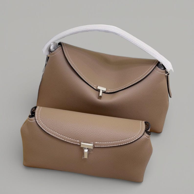 Pu&ograve; includere: Due borse color taupe. La borsa pi&ugrave; grande ha un manico bianco e una chiusura a patta con chiusura color argento. La borsa pi&ugrave; piccola ha un design simile, con chiusura a patta e chiusura color argento.