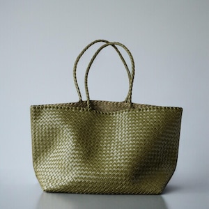 May include: A woven olive green tote bag with two braided handles. The bag has a rectangular shape and a textured surface. The handles are attached to the top of the bag and are made of the same material as the bag.